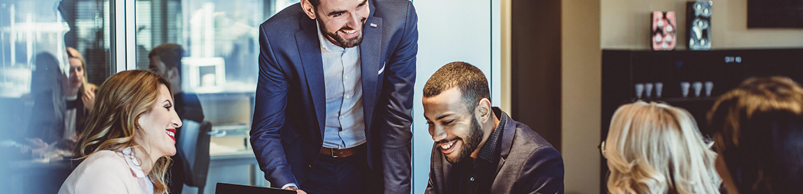 A business conference room with a group of professionals seated at a table talking and smiling. 