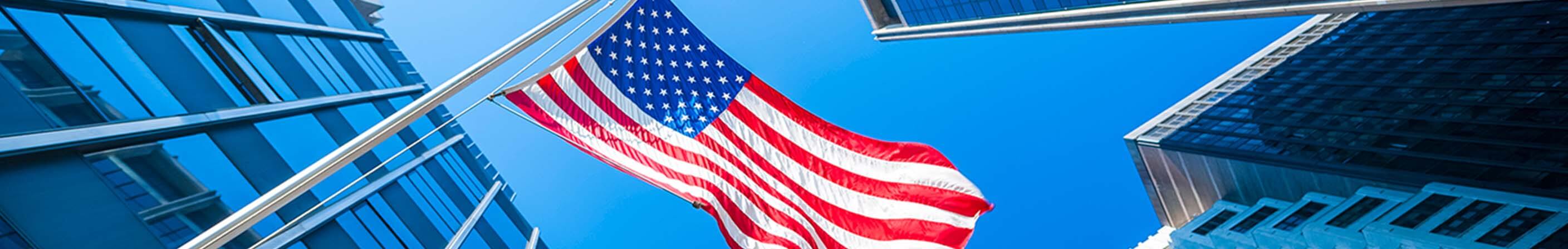 American flag against blue sky between modern buildings