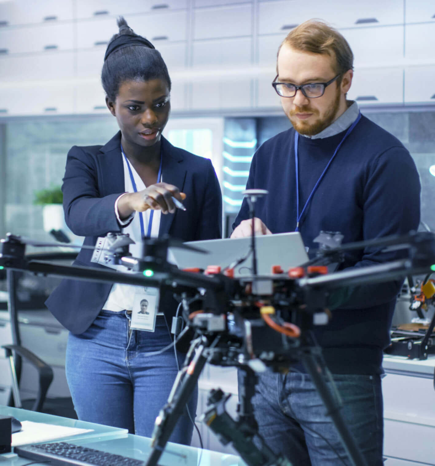 A black woman and Caucasian man working together on a drone in a lab.