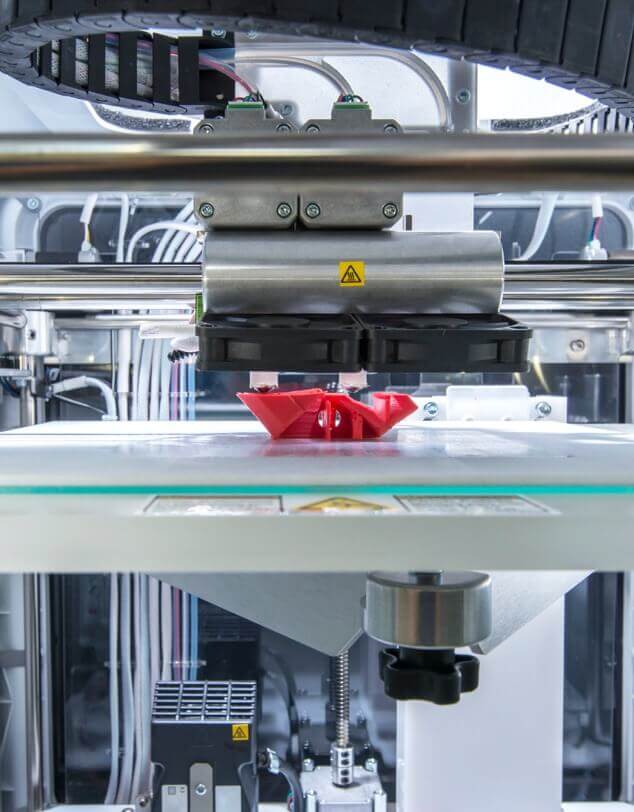 A 3D printer in the process of printing a red plastic component. 