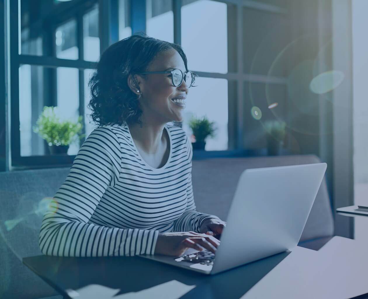A black woman in glasses at her computer screen smiling. 