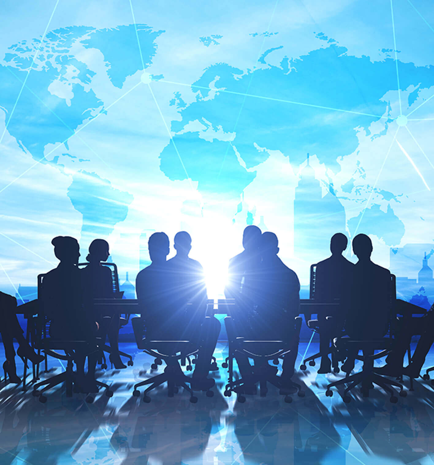 A silhouetted group of business people seated at a meeting table with an image of the world illuminated behind them. 