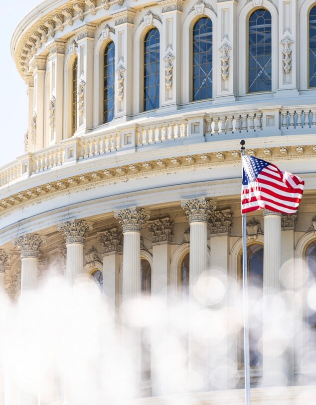 A small American flag waving against the U.S. Capitol building,