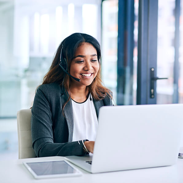 A young dark-haired woman smiling as she types on a laptop.