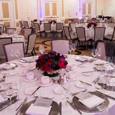 Closeup of a formal event dinner table set with programs and floral arrangements. 