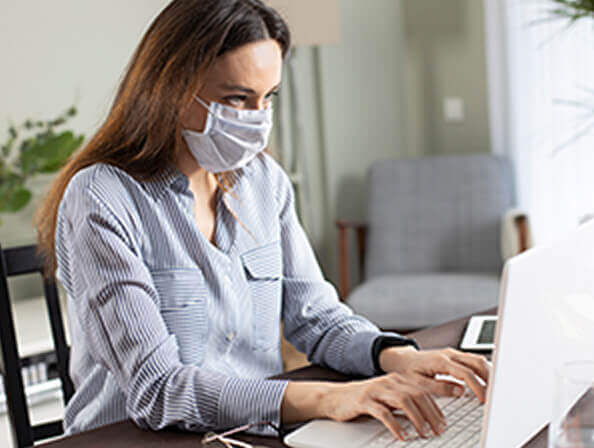 A female office worker wears a mask as she looks at her computer screen.